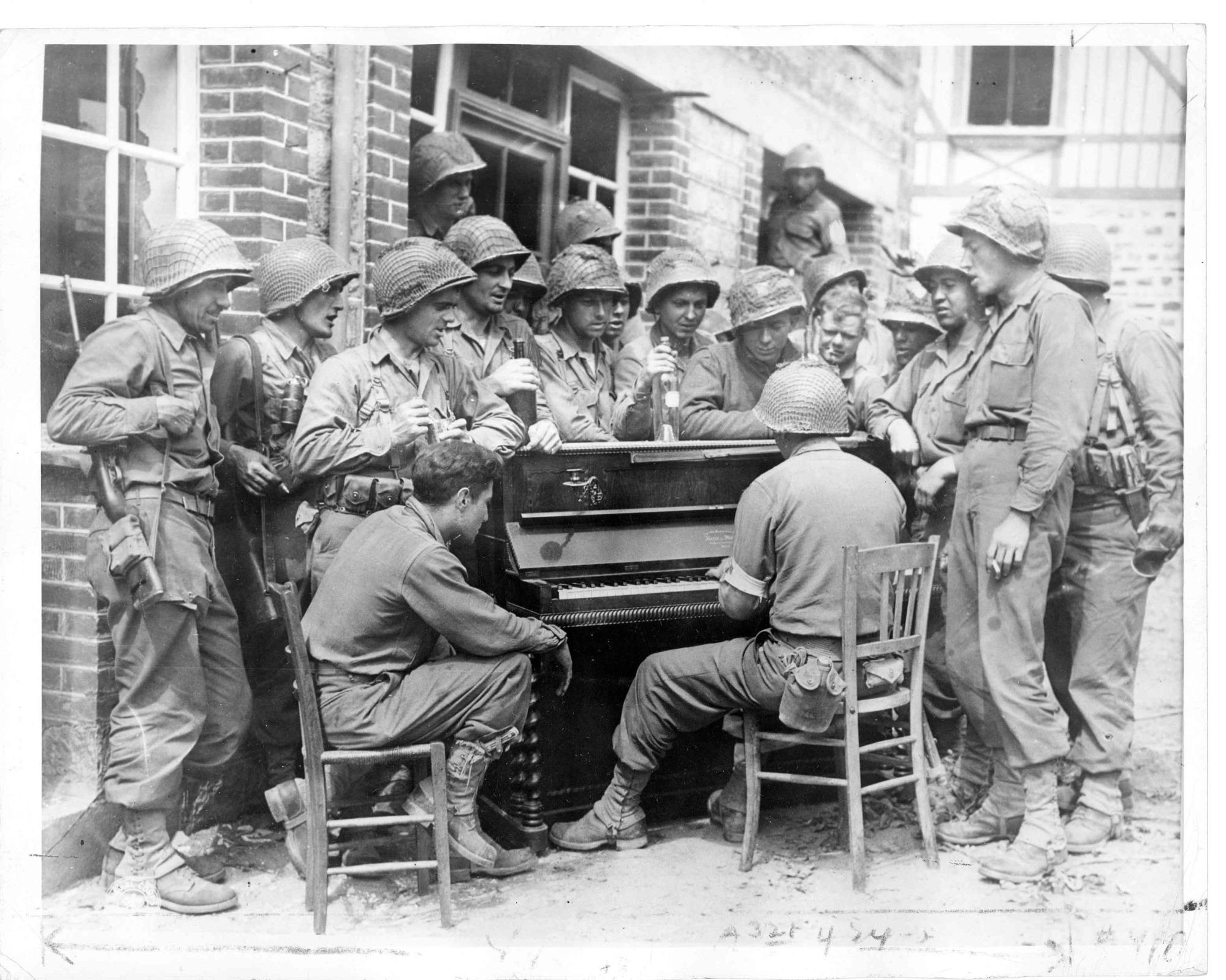 Soldats américains regroupés autour d'un piano, dans une rue de Barenton. 